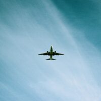 A commercial airplane is flying overhead against a blue sky with wispy white clouds and contrails.