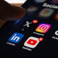 A smartphone screen displays social media apps: X with 21 notifications, Instagram, TikTok, LinkedIn, and YouTube with 9 notifications, under a Social Media folder.