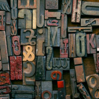 A collection of vintage wooden letterpress type blocks in various sizes, shapes, and colors arranged closely together, showing letters, numbers, and symbols.