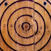 A hand-drawn black target with concentric circles and numbers is painted on wooden planks, used for axe or knife throwing.