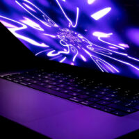Laptop open in a dark room displaying a glowing, abstract purple and white tunnel animation on the screen.
