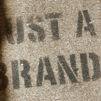 The words JUST A BRAND spray-painted on a textured surface.